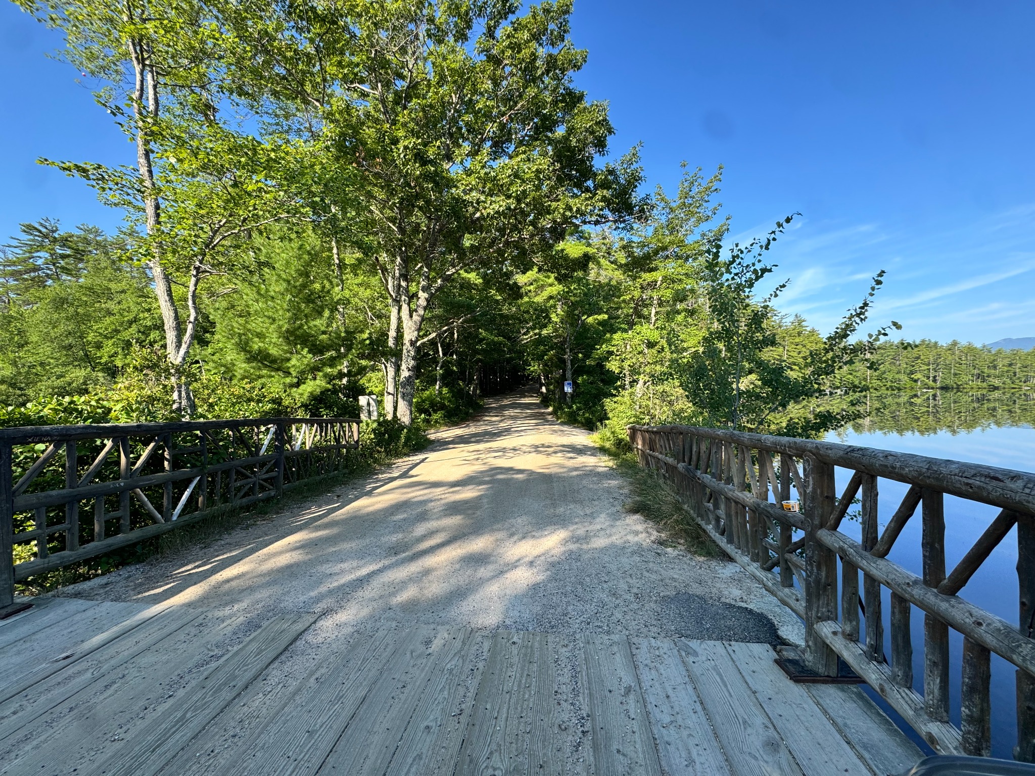 Gravel road continuing from a rustic timber bridge into sunlit forest